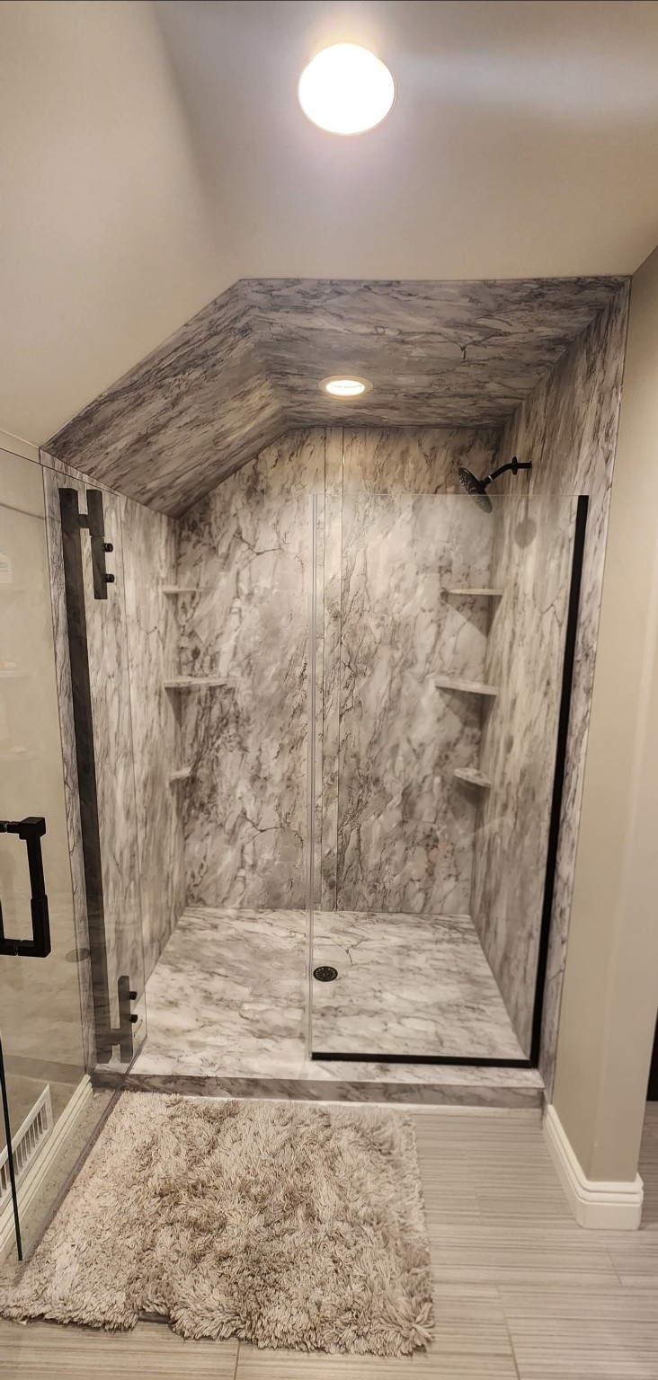After: marble-pattern walk-in shower with glass enclosure beneath a sloped ceiling