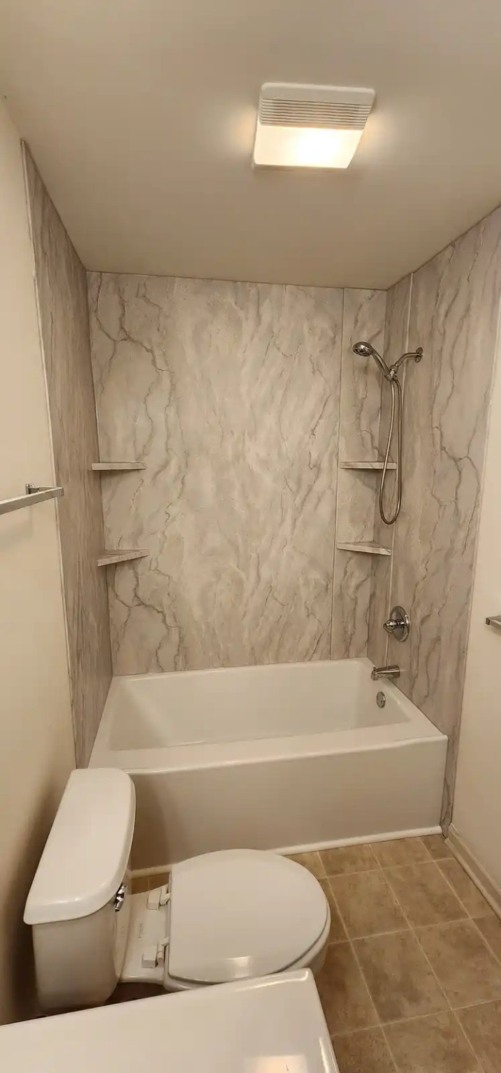 Bathtub installation with marble-look acrylic surround and corner shelves