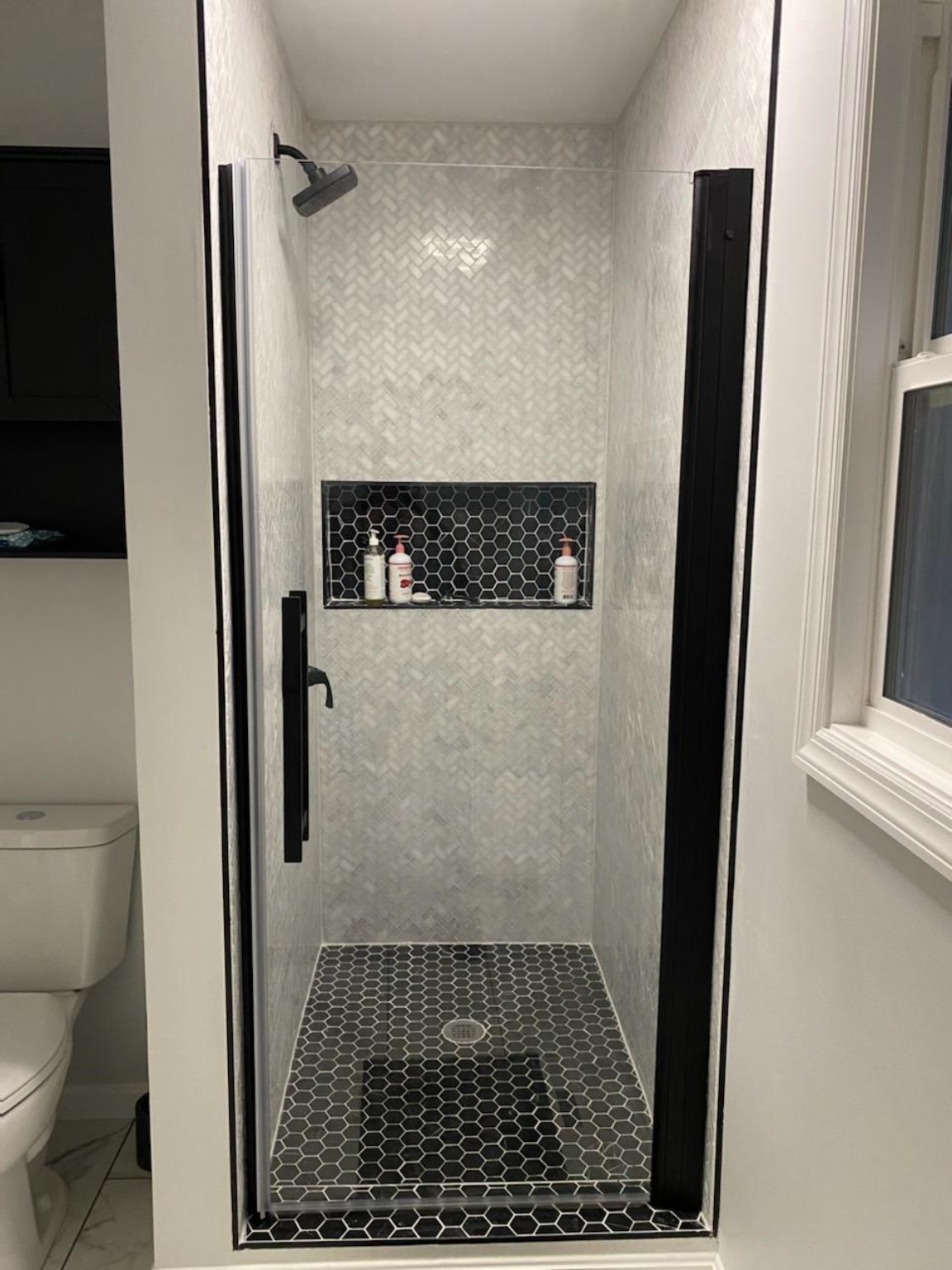 Enlarged tiled shower with black hexagonal floor, recessed niche and glass door